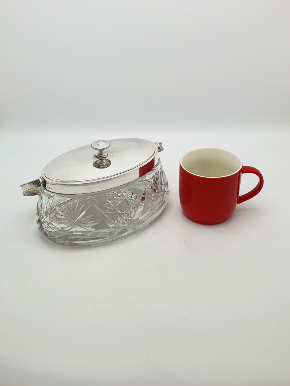 An oval cut glass biscuit box featuring a starburst motif, fitted with a silver-plated lid, central finial, and a beaded swing handle. View IX