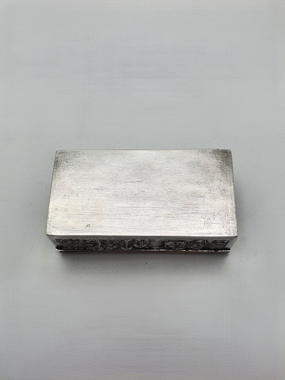 A rectangular antique silver trinket box featuring detailed repousse relief depicting a village scene with huts and palm trees. View VIII