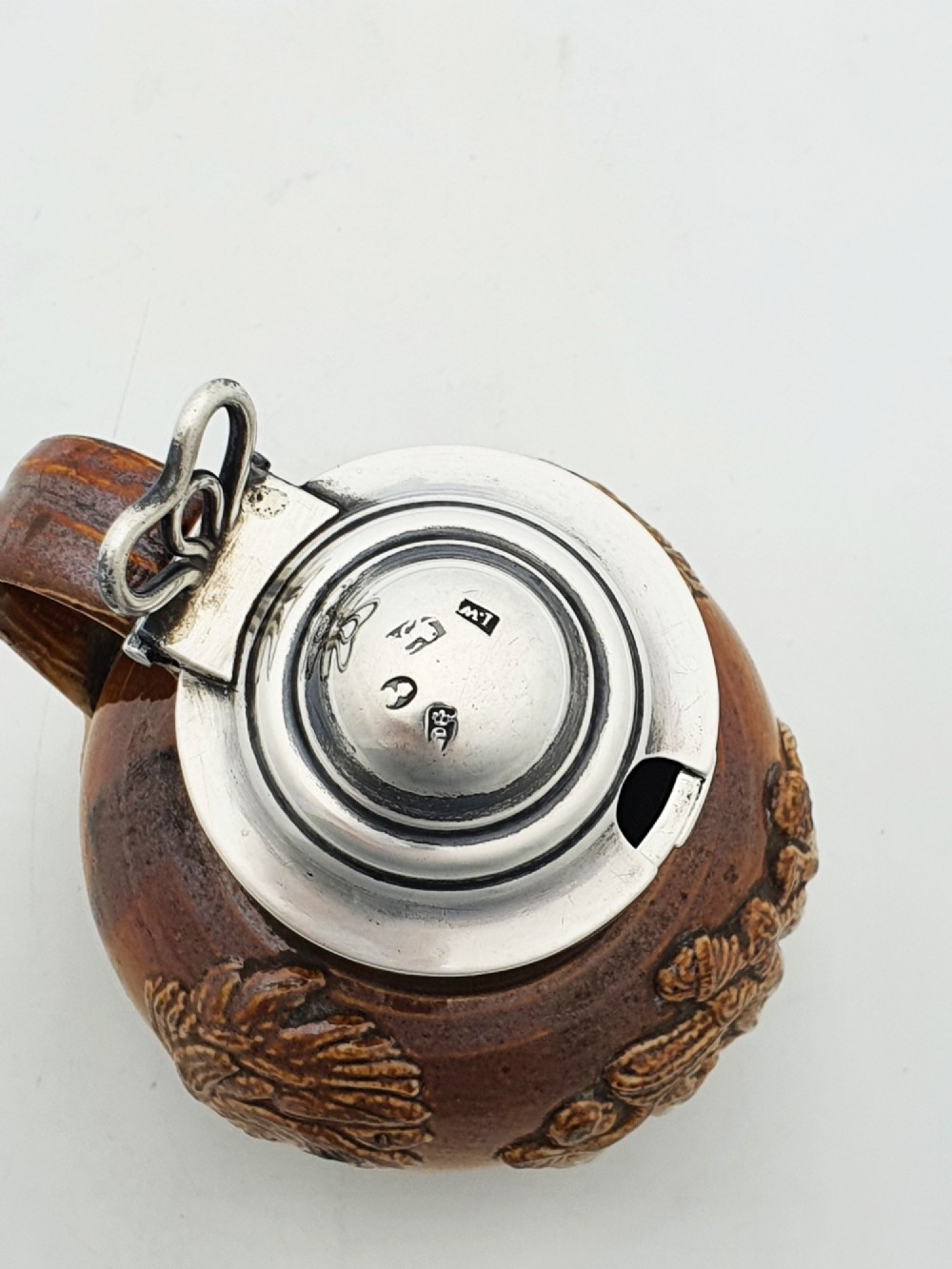 A small salt-glazed brown and beige stoneware jug featuring relief motifs and a hallmarked sterling silver hinged lid and collar. View VII