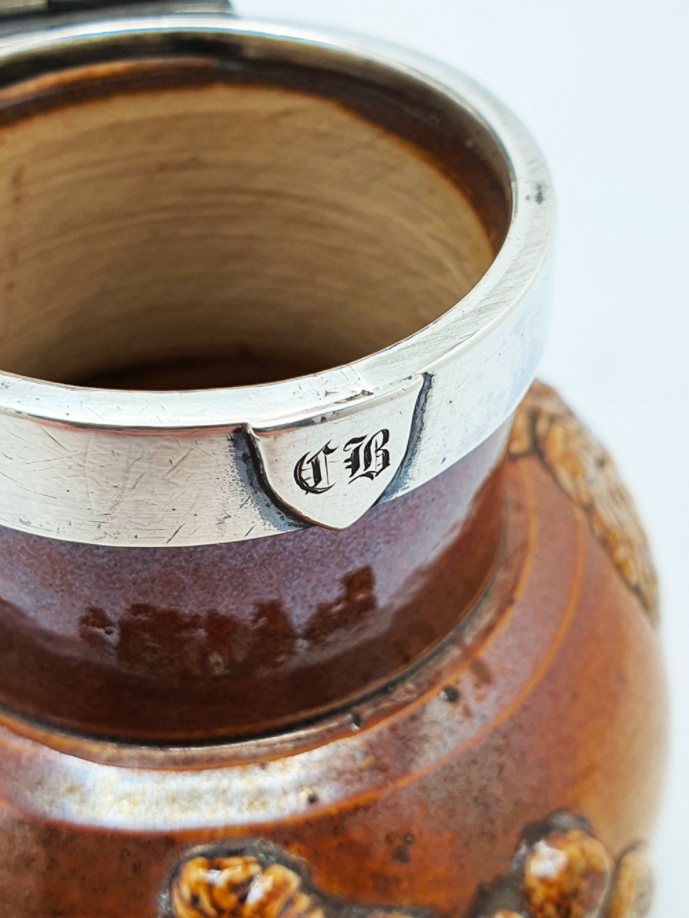 A small salt-glazed brown and beige stoneware jug featuring relief motifs and a hallmarked sterling silver hinged lid and collar. View XI