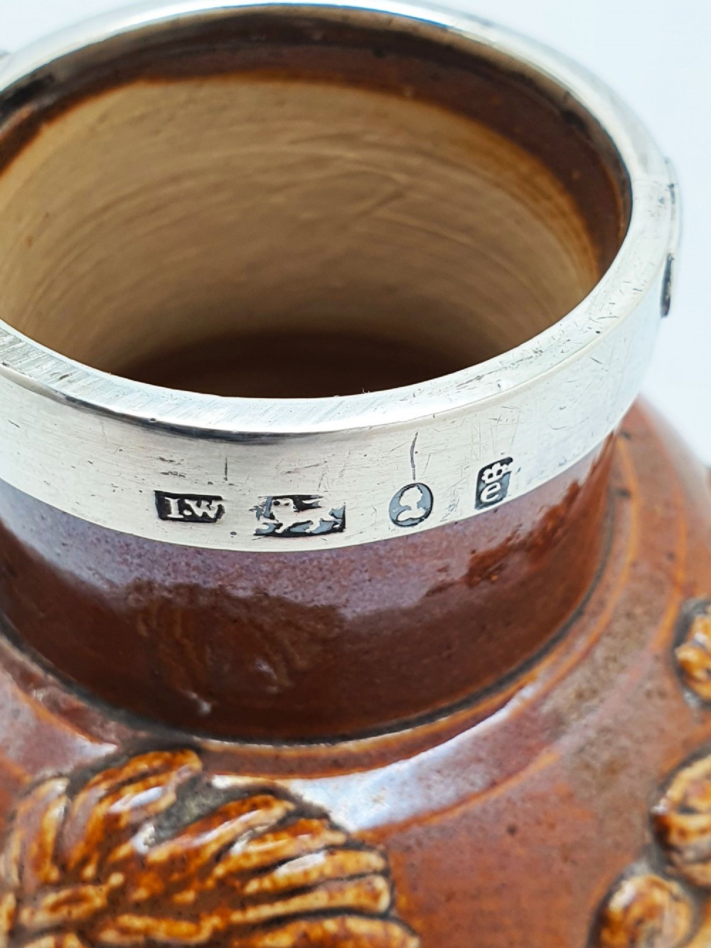 A small salt-glazed brown and beige stoneware jug featuring relief motifs and a hallmarked sterling silver hinged lid and collar. View XIII