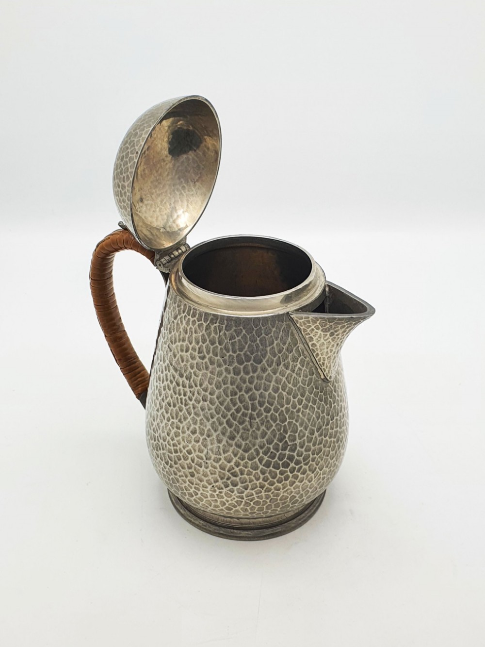 A planished pewter coffee pot featuring a domed lid, triangular spout, and a brown cane-wrapped handle. View II