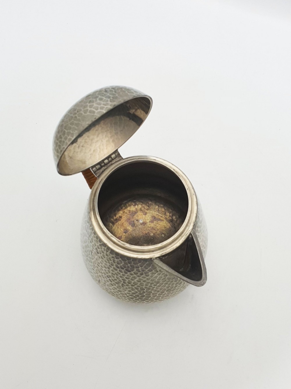 A planished pewter coffee pot featuring a domed lid, triangular spout, and a brown cane-wrapped handle. View III