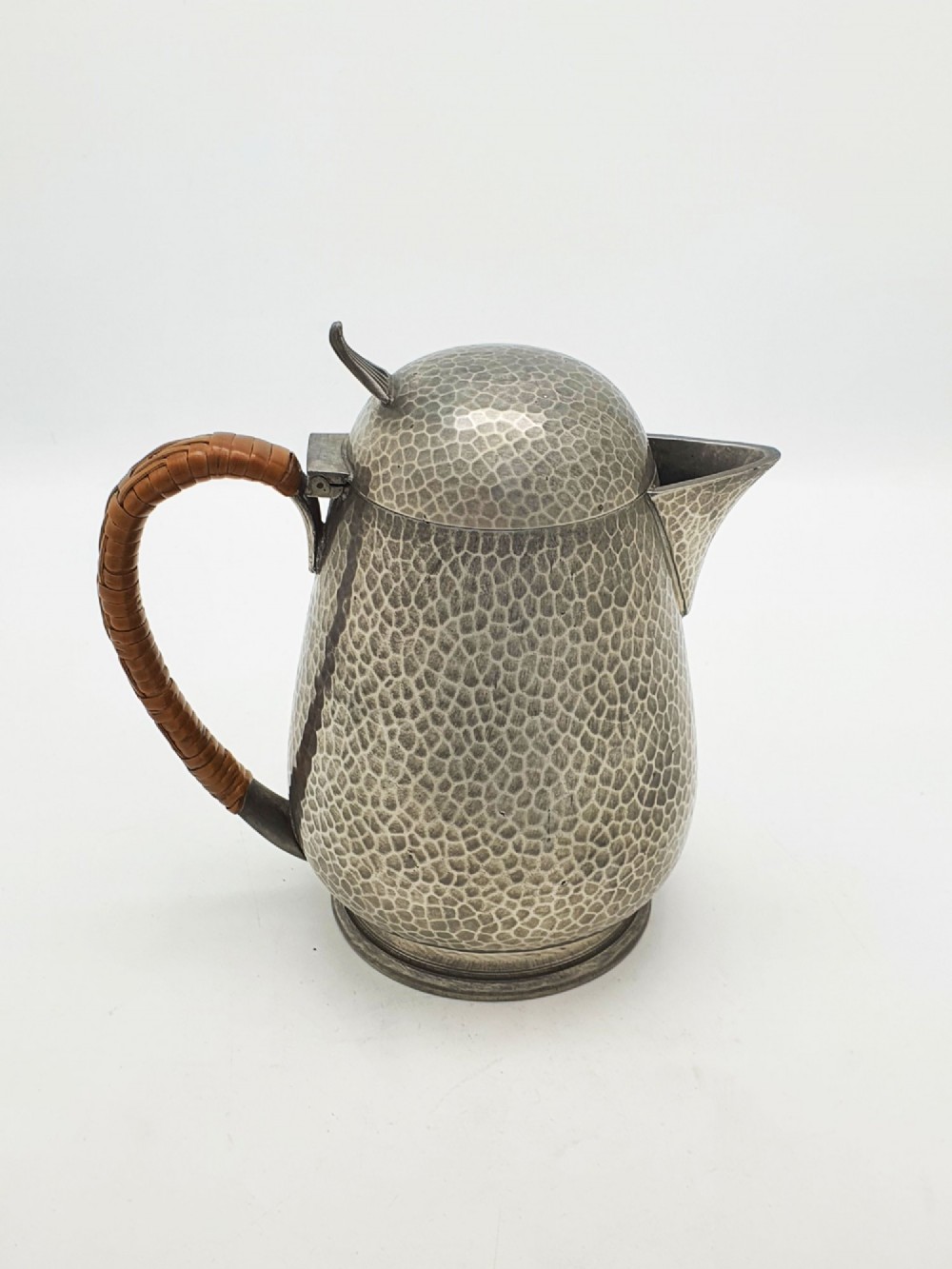 A planished pewter coffee pot featuring a domed lid, triangular spout, and a brown cane-wrapped handle. View IV