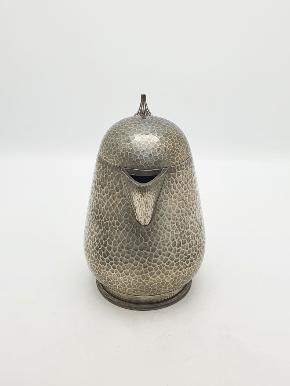 A planished pewter coffee pot featuring a domed lid, triangular spout, and a brown cane-wrapped handle. View V