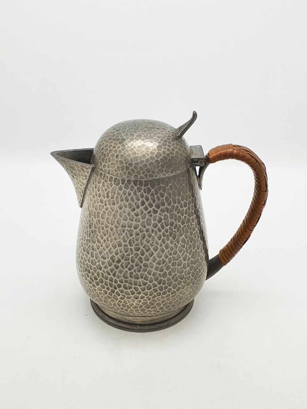 A planished pewter coffee pot featuring a domed lid, triangular spout, and a brown cane-wrapped handle. View VI