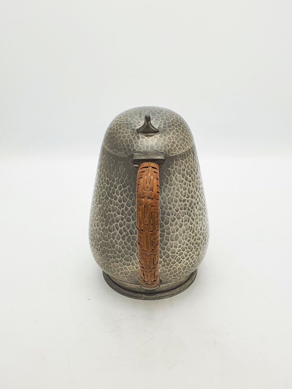 A planished pewter coffee pot featuring a domed lid, triangular spout, and a brown cane-wrapped handle. View VII