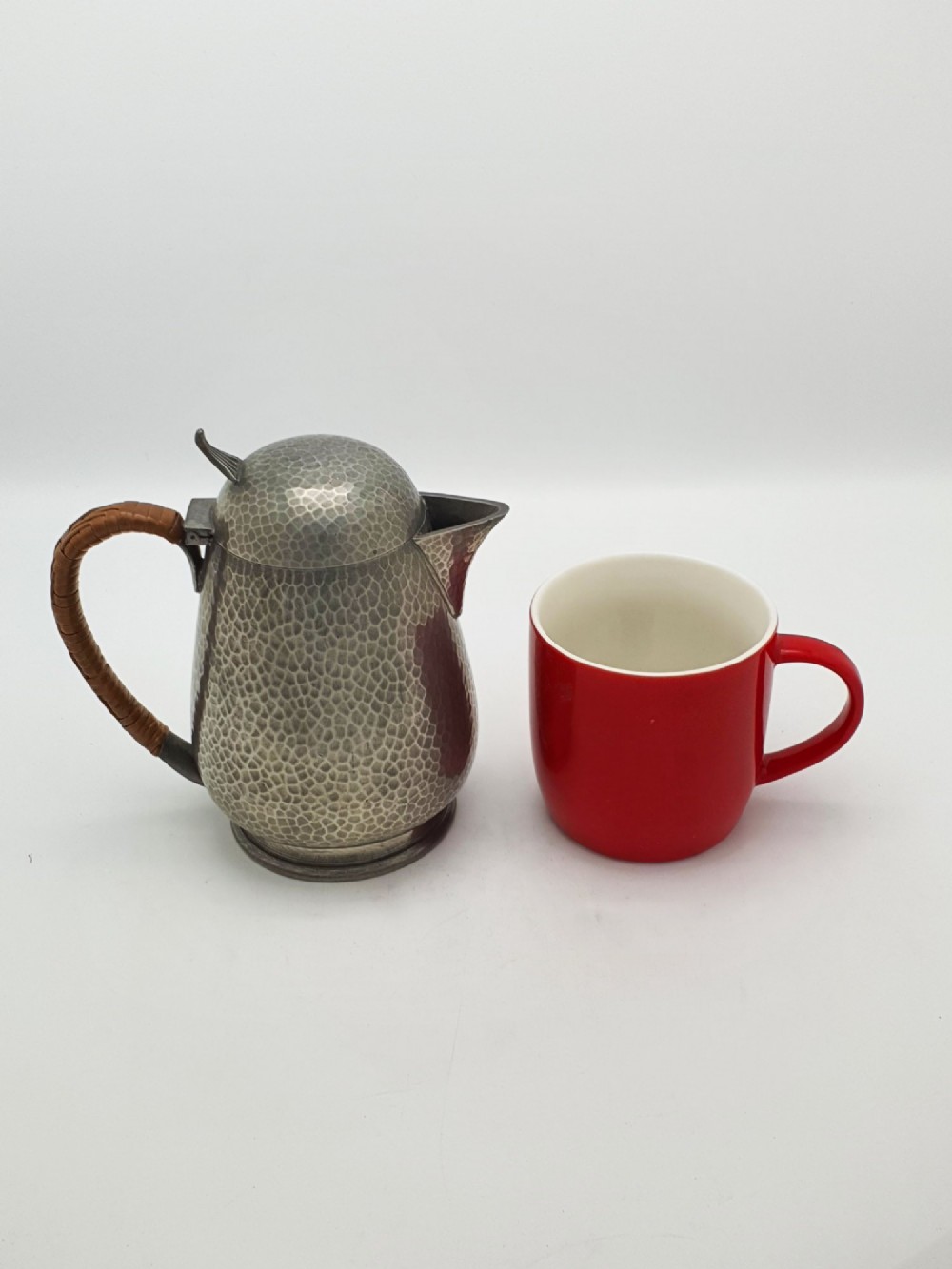 A planished pewter coffee pot featuring a domed lid, triangular spout, and a brown cane-wrapped handle. View IX