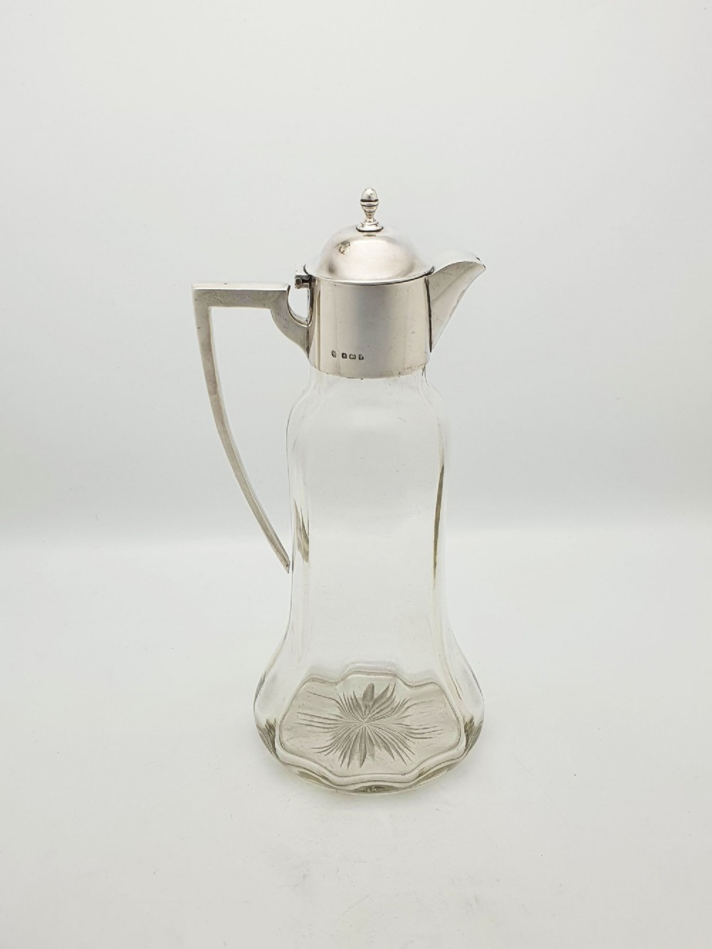 An Edwardian clear glass claret jug featuring a star-cut base, fluted body, angular silver handle, and sterling silver mounted spout with a domed lid. View II