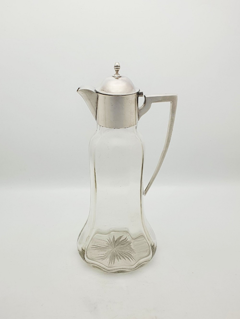 An Edwardian clear glass claret jug featuring a star-cut base, fluted body, angular silver handle, and sterling silver mounted spout with a domed lid. View III