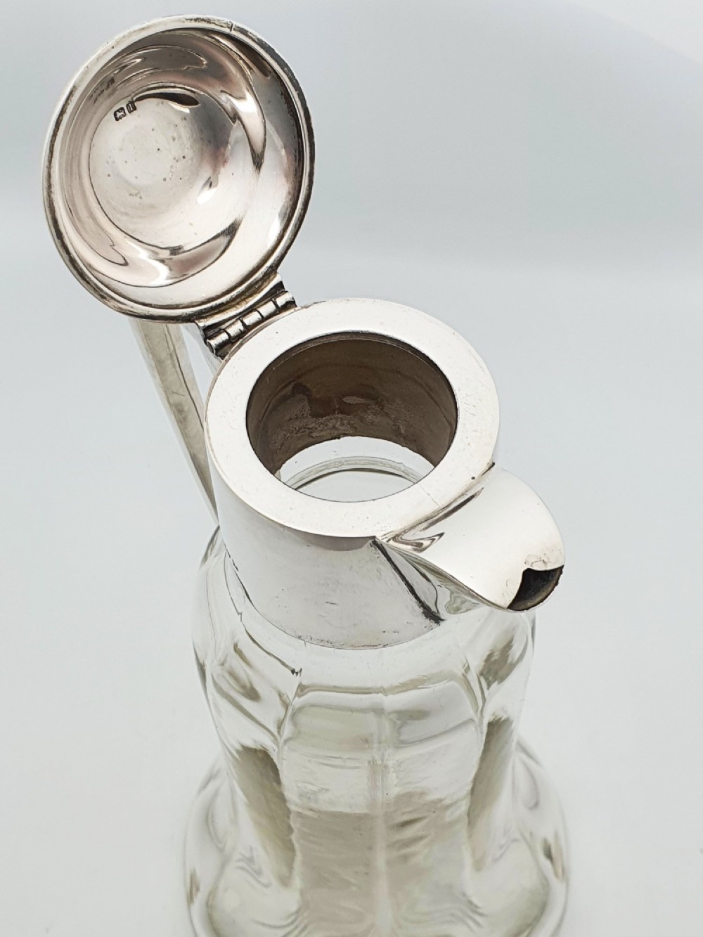 An Edwardian clear glass claret jug featuring a star-cut base, fluted body, angular silver handle, and sterling silver mounted spout with a domed lid. View IV