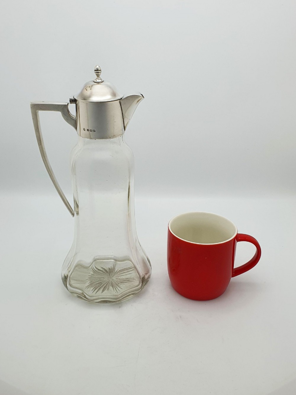 An Edwardian clear glass claret jug featuring a star-cut base, fluted body, angular silver handle, and sterling silver mounted spout with a domed lid. View VIII