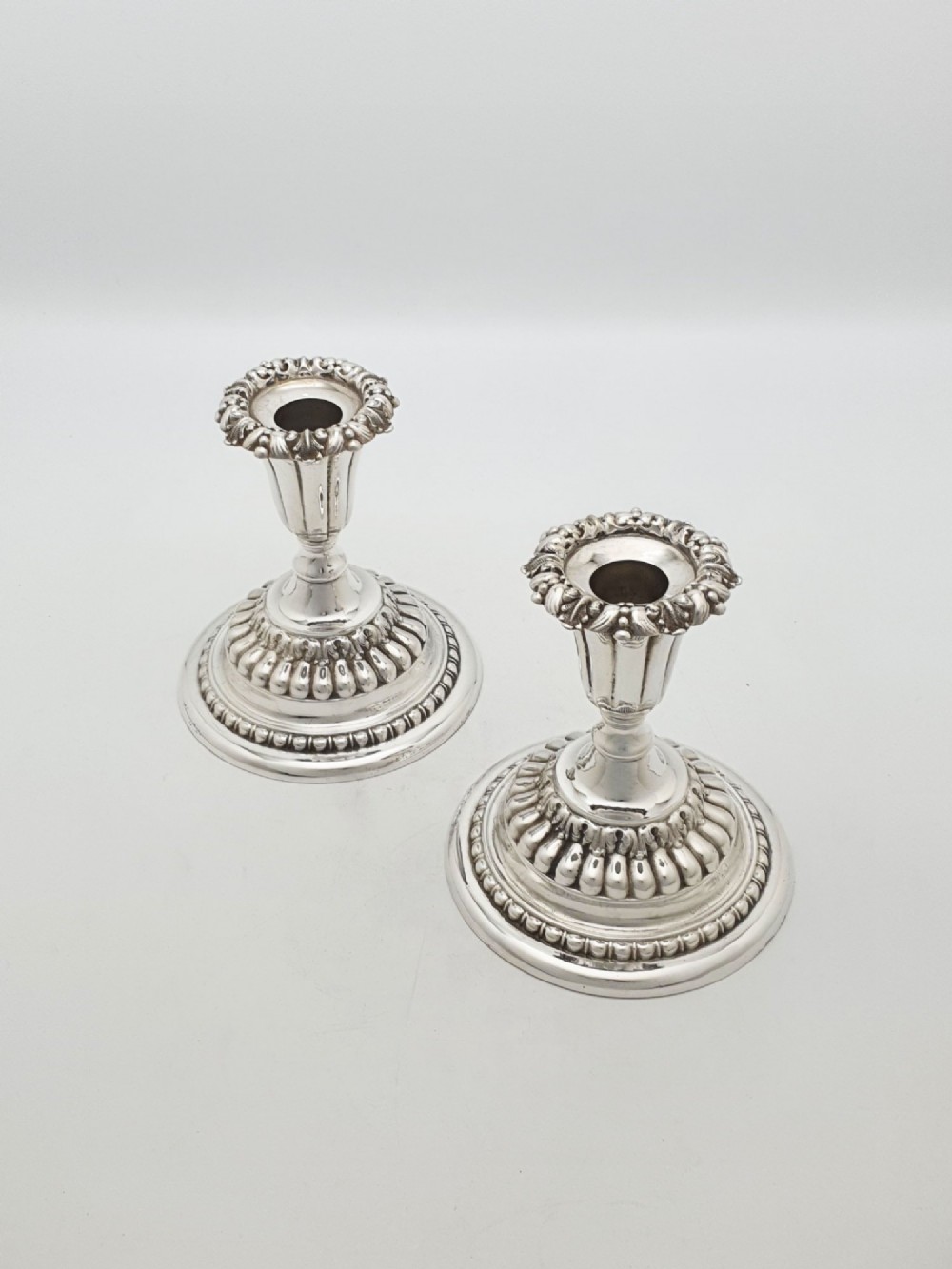 A pair of antique Edwardian low silver-plated candlesticks featuring fluted sockets and gadrooned circular bases.