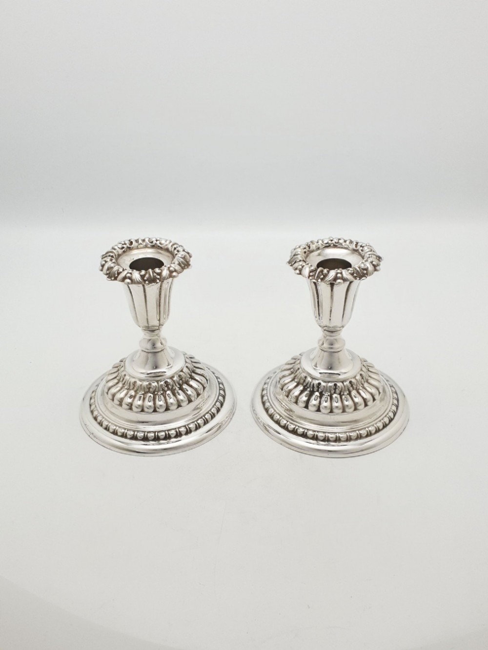 A pair of antique Edwardian low silver-plated candlesticks featuring fluted sockets and gadrooned circular bases. View II