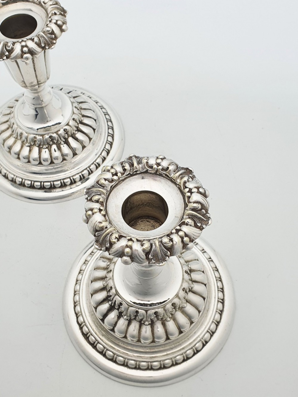A pair of antique Edwardian low silver-plated candlesticks featuring fluted sockets and gadrooned circular bases. View V