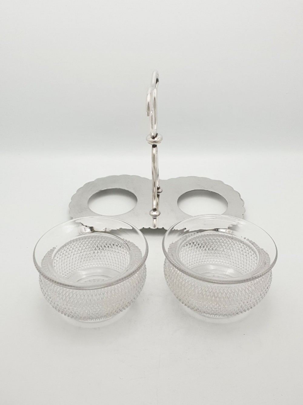 A silver-plated condiment stand featuring a central looped handle, ball feet, and two clear diamond-patterned glass bowls. View II