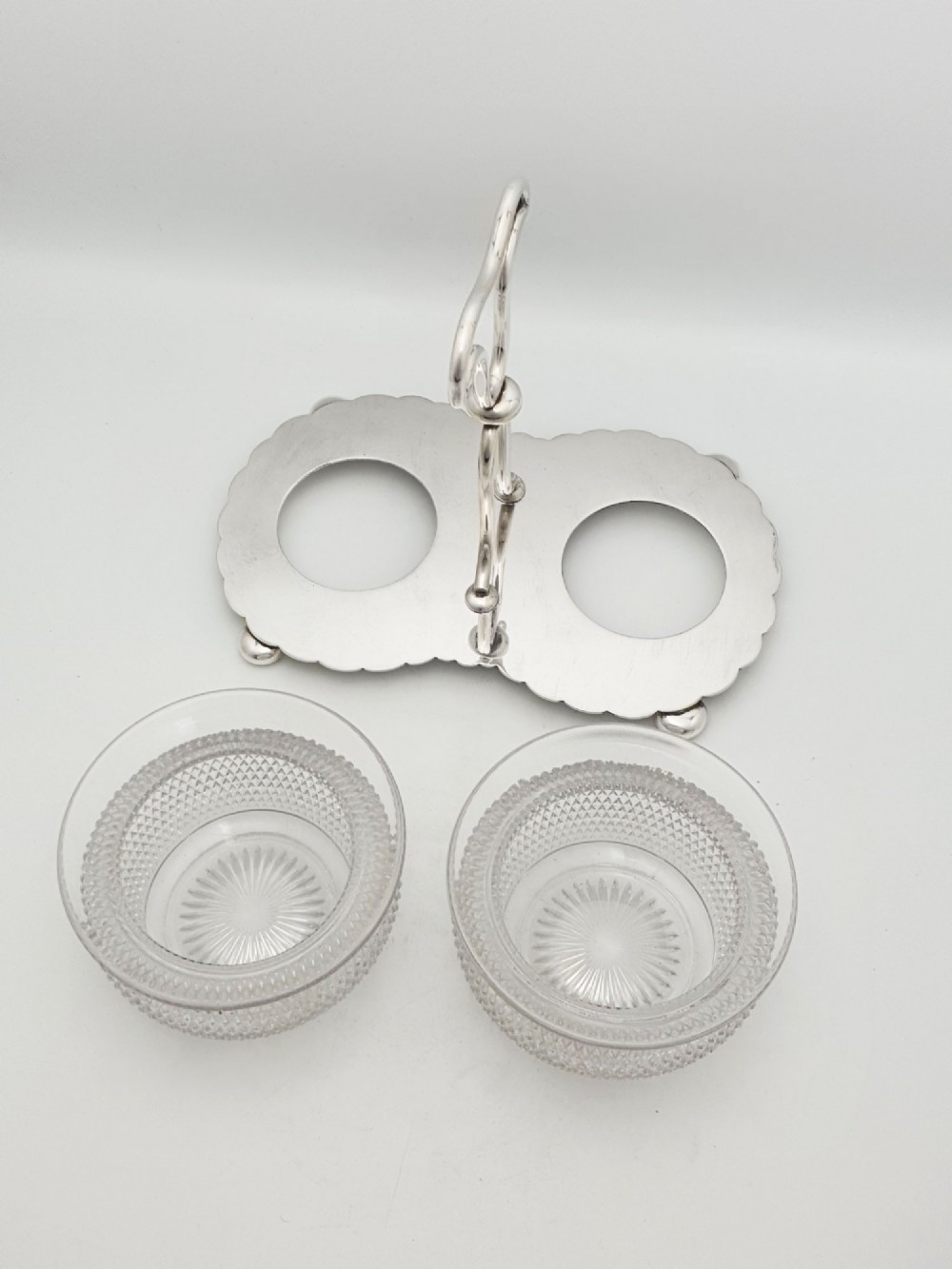 A silver-plated condiment stand featuring a central looped handle, ball feet, and two clear diamond-patterned glass bowls. View III