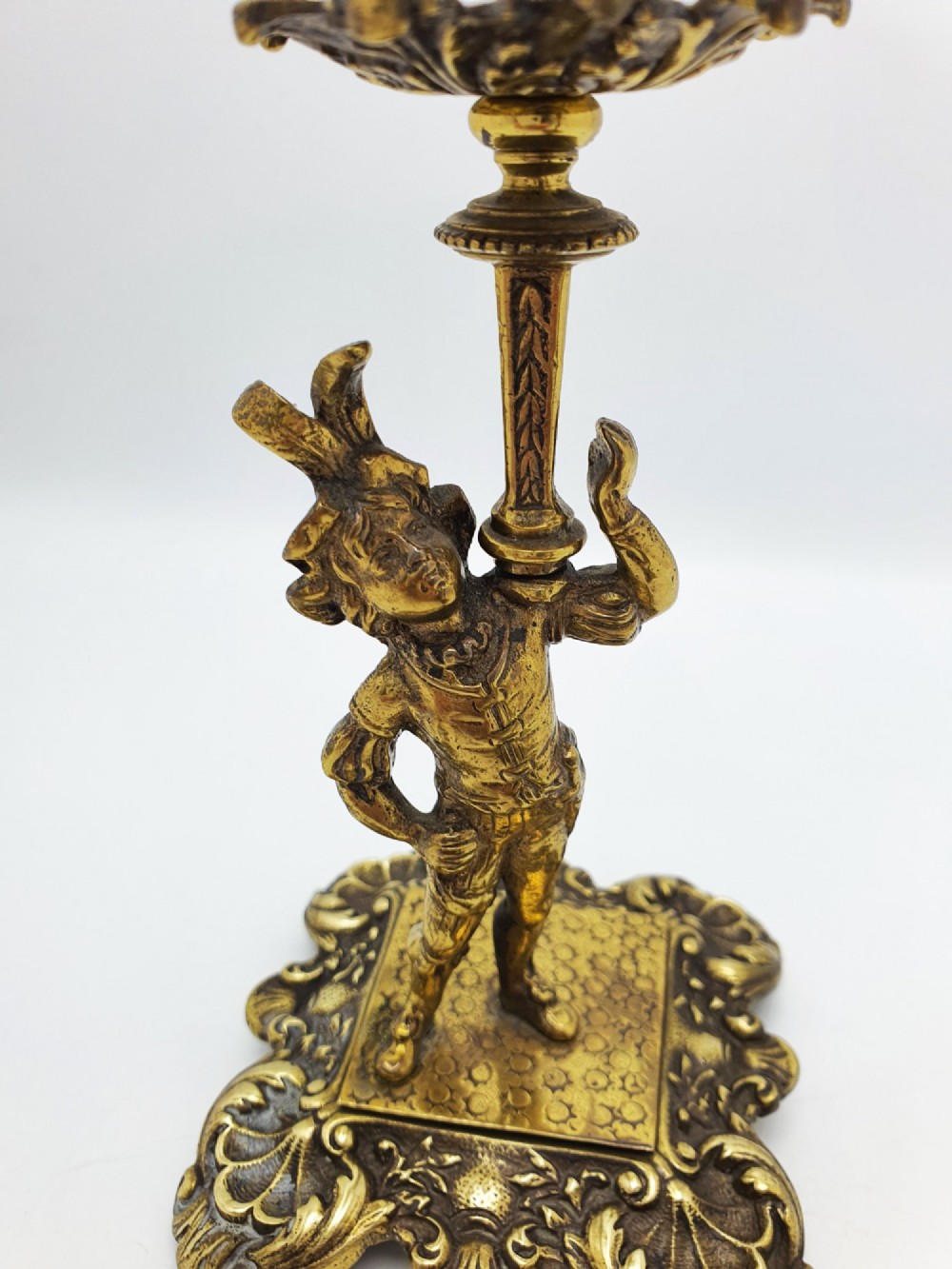 A pair of Victorian gilt brass candlesticks featuring sculpted figural stems raised on square ornamented bases with acanthus detail. View III
