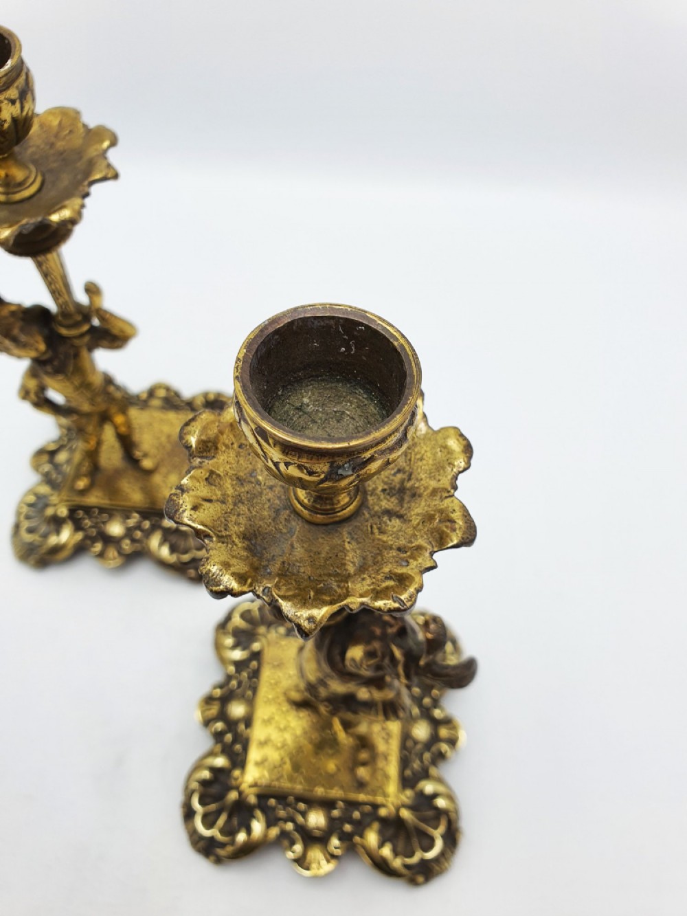 A pair of Victorian gilt brass candlesticks featuring sculpted figural stems raised on square ornamented bases with acanthus detail. View IV