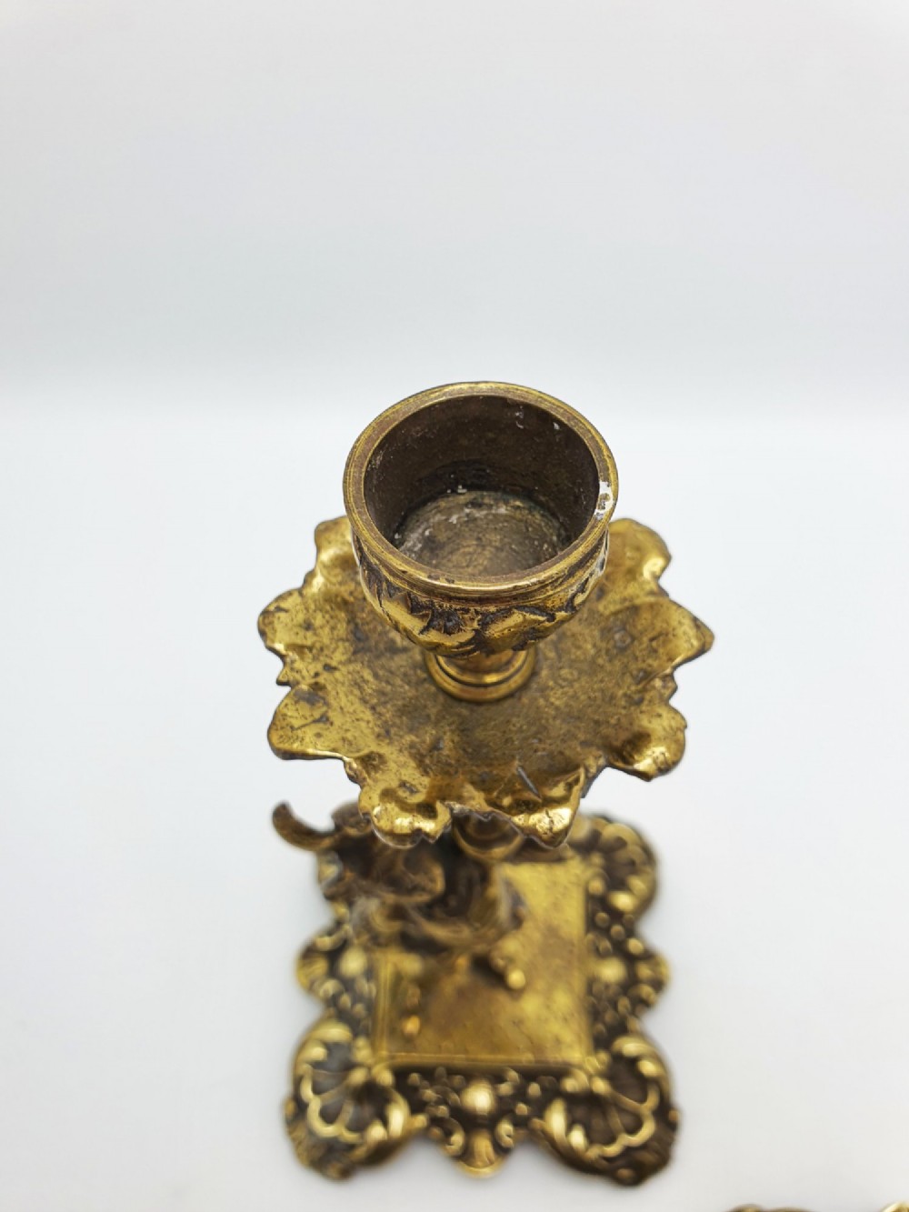 A pair of Victorian gilt brass candlesticks featuring sculpted figural stems raised on square ornamented bases with acanthus detail. View V