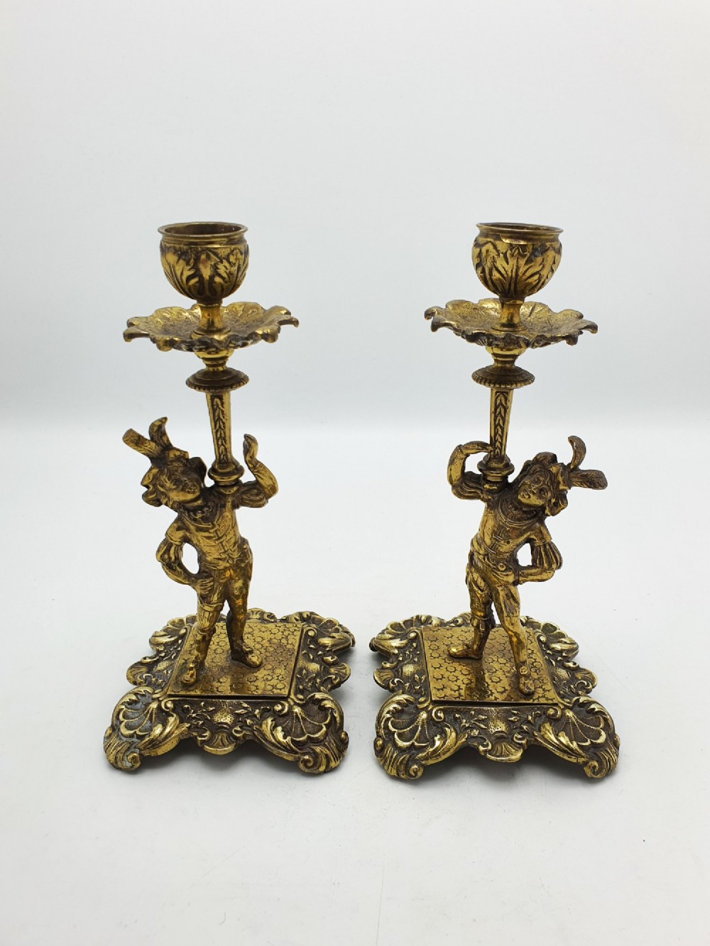 A pair of Victorian gilt brass candlesticks featuring sculpted figural stems raised on square ornamented bases with acanthus detail. View VI