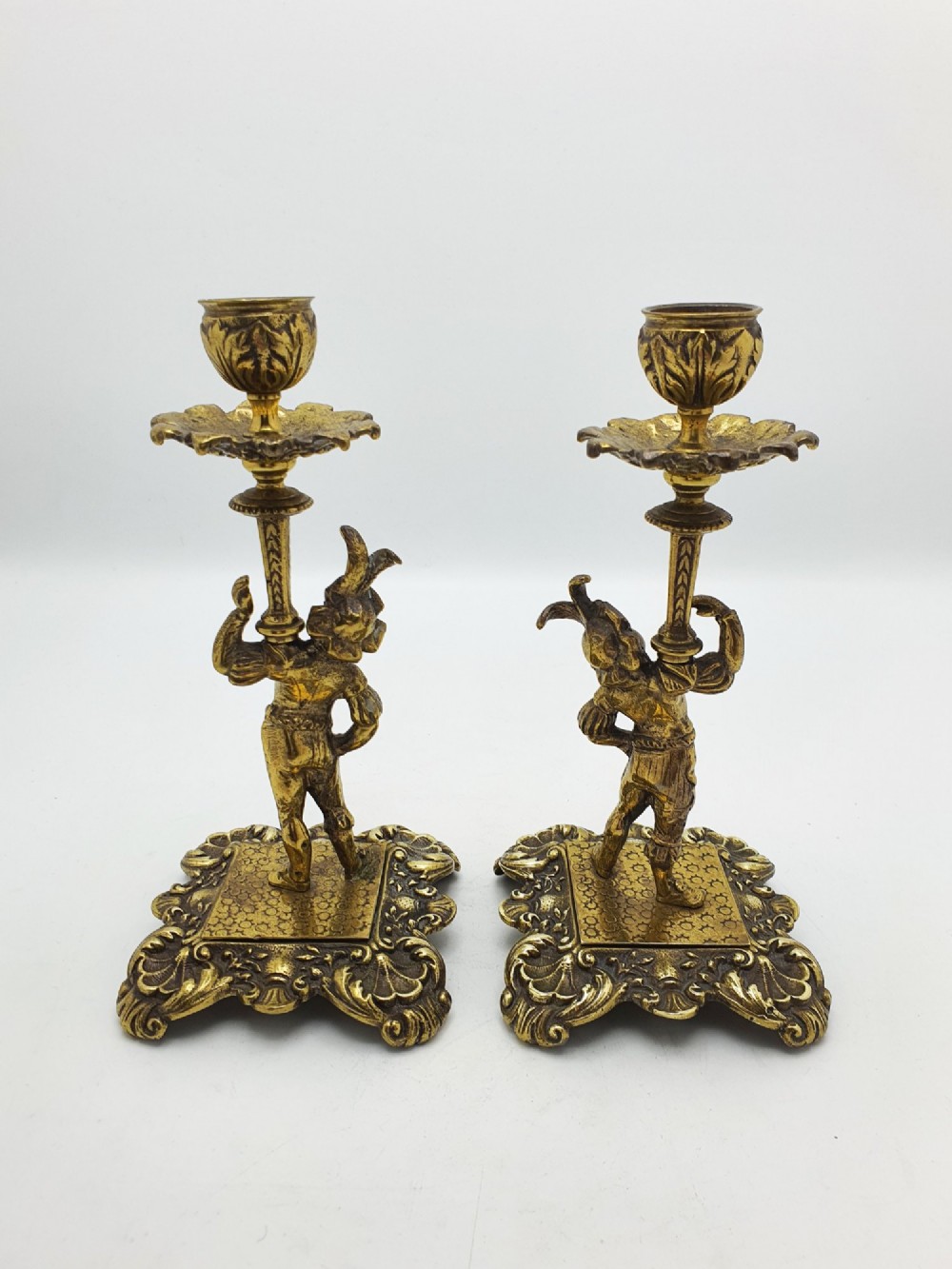 A pair of Victorian gilt brass candlesticks featuring sculpted figural stems raised on square ornamented bases with acanthus detail. View VII