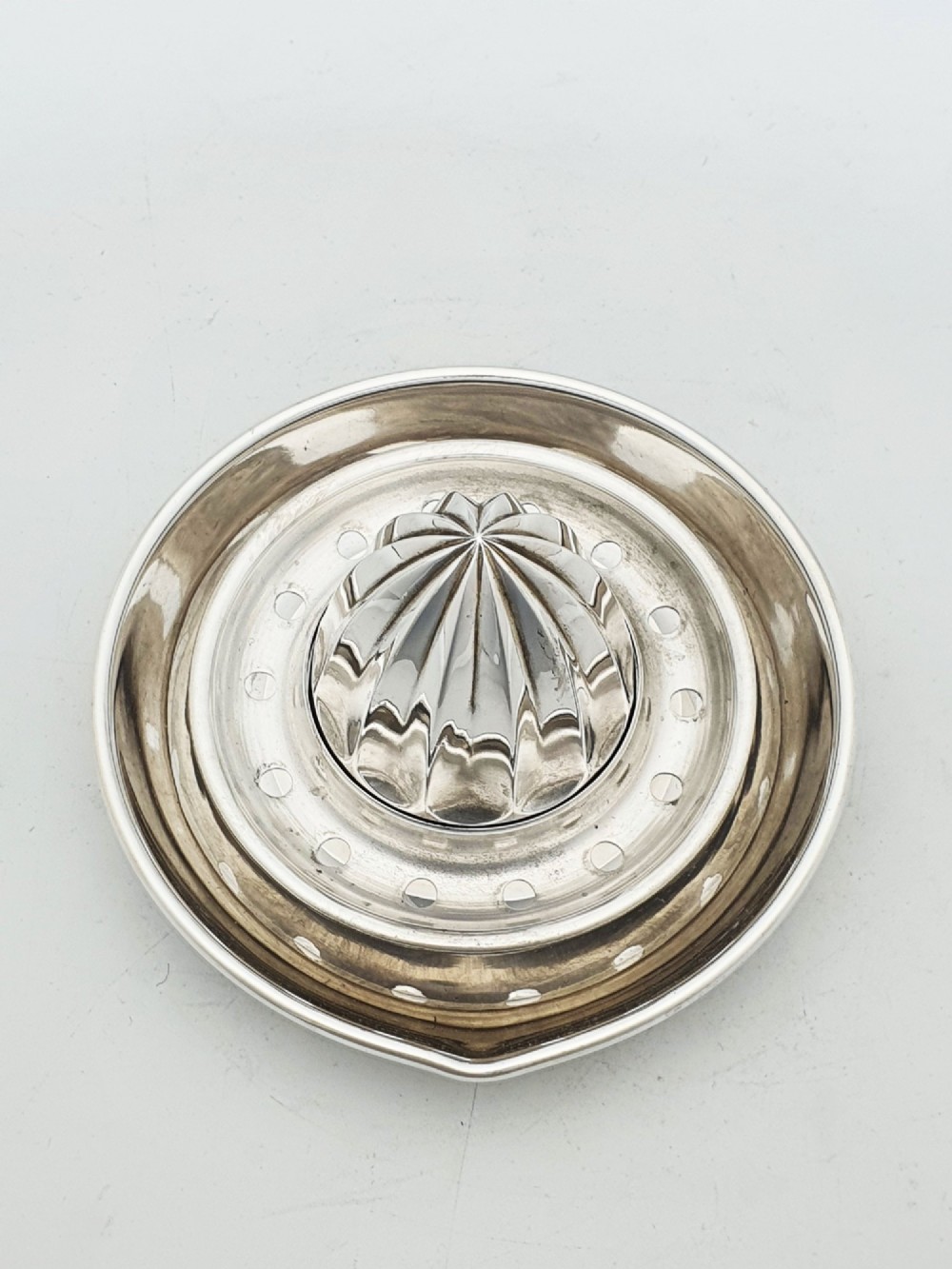 A silver-plated manual citrus squeezer featuring a central fluted reamer cone, a circular perforated strainer ring, and a shallow catch tray. View II
