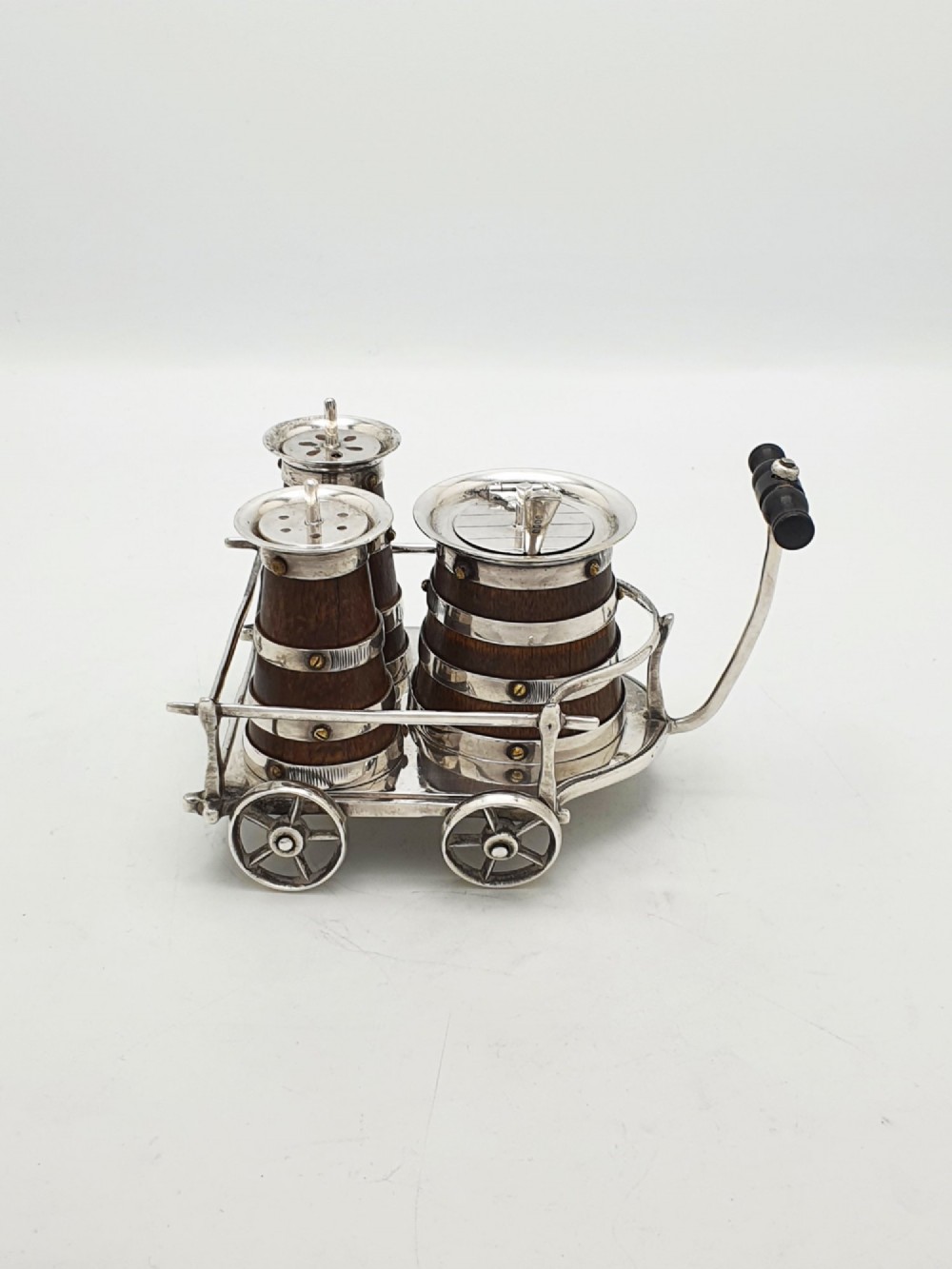 An antique Victorian silver-plated condiment set crafted as a miniature four-wheeled trolley holding three oak barrel-shaped containers. View II