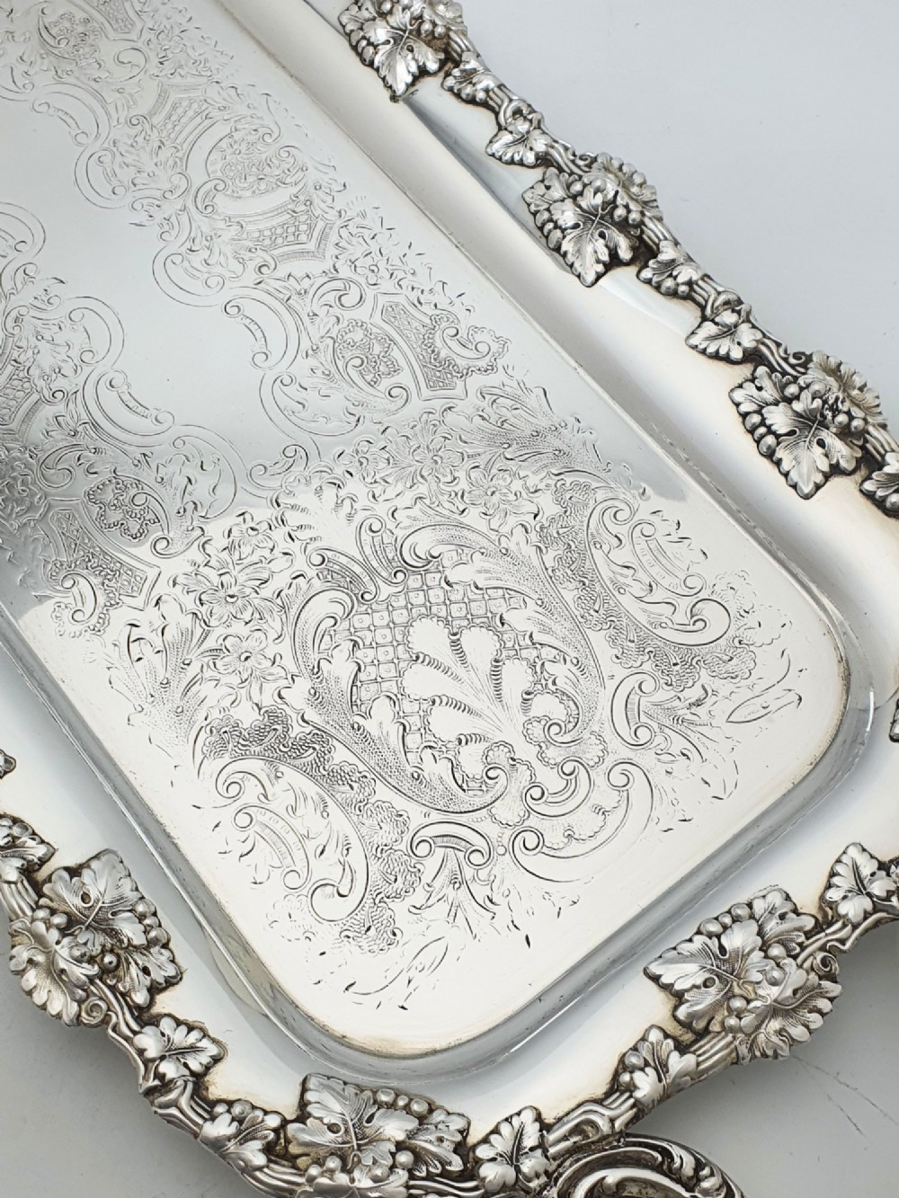 A long rectangular silver plated serving tray featuring an ornate grapevine motif rim, twin cast scroll handles, and an intricately chased floral central surface pattern. View III