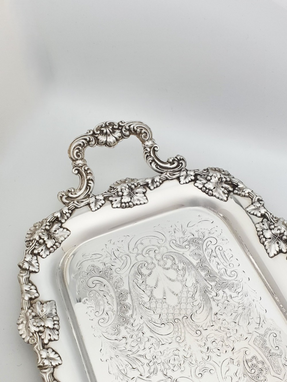 A long rectangular silver plated serving tray featuring an ornate grapevine motif rim, twin cast scroll handles, and an intricately chased floral central surface pattern. View IV