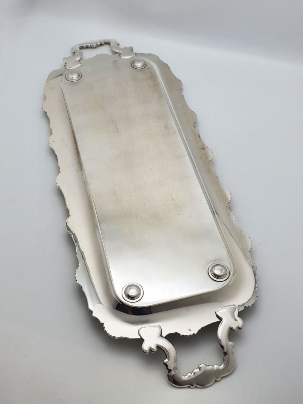 A long rectangular silver plated serving tray featuring an ornate grapevine motif rim, twin cast scroll handles, and an intricately chased floral central surface pattern. View VII