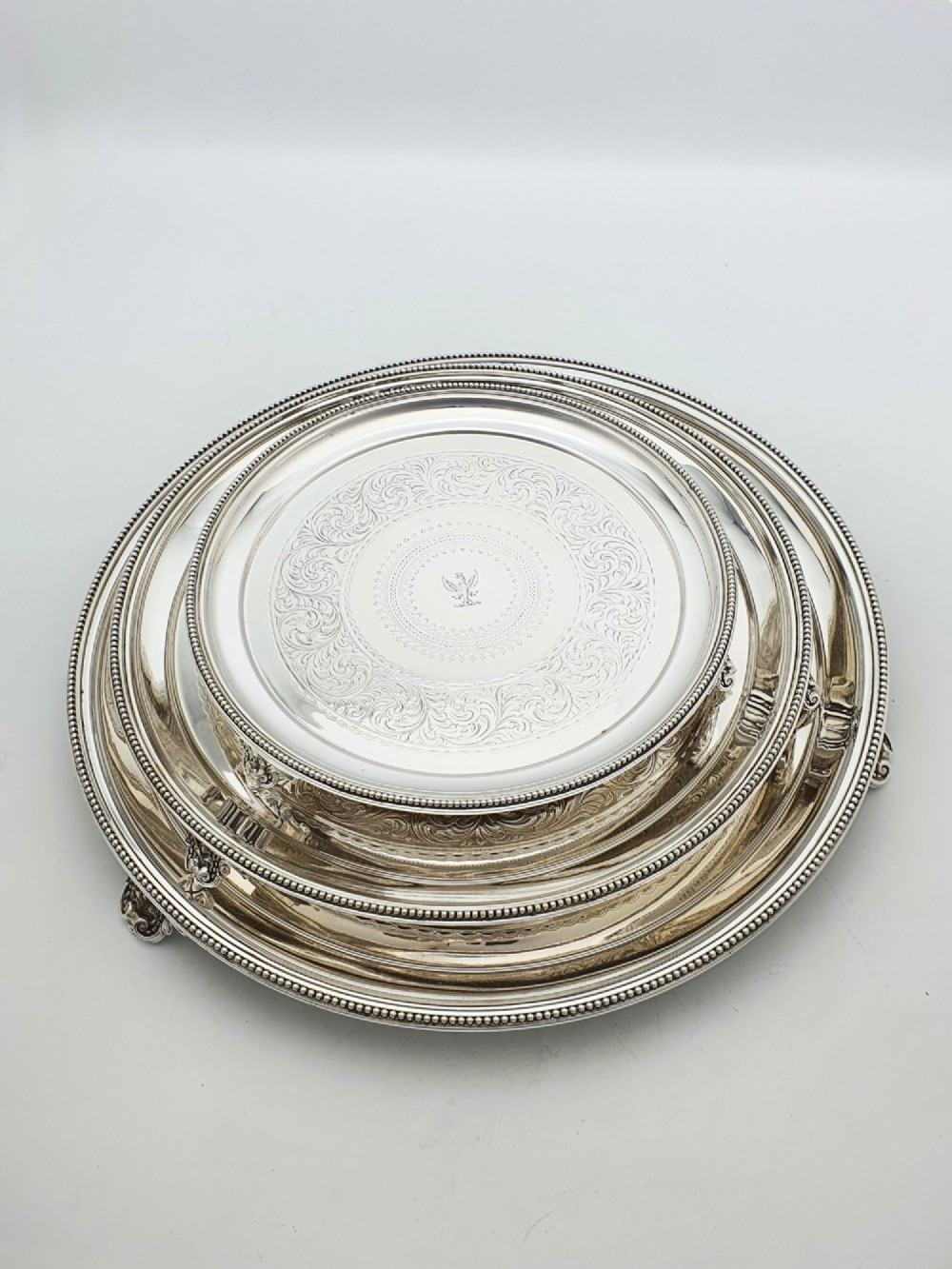 A set of three circular Victorian silver plated salvers arranged in graduated sizes, featuring beaded borders, detailed scroll engraving, and central crests. View III