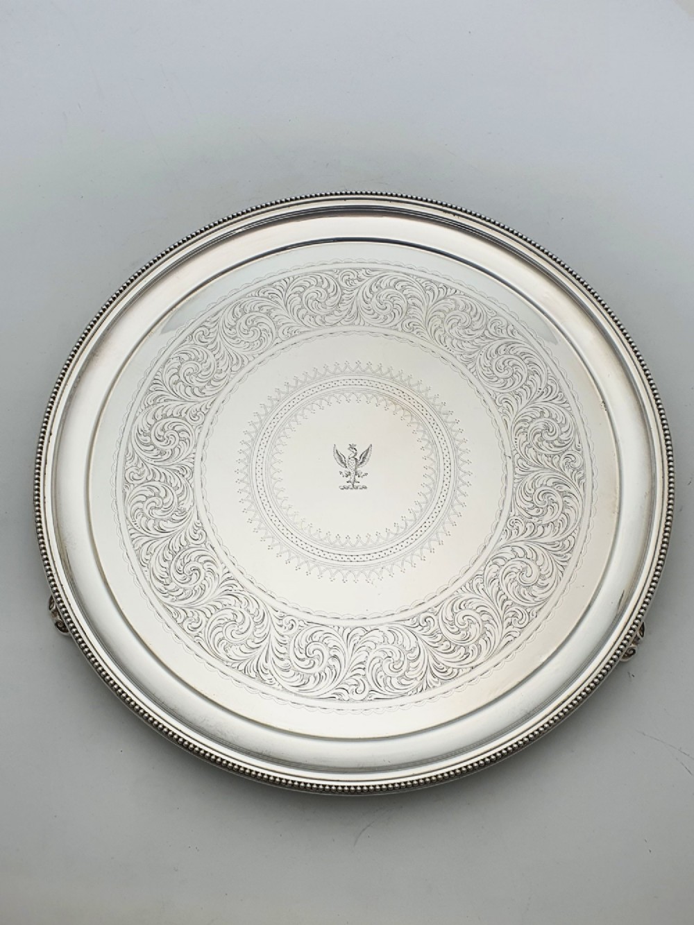 A set of three circular Victorian silver plated salvers arranged in graduated sizes, featuring beaded borders, detailed scroll engraving, and central crests. View IV