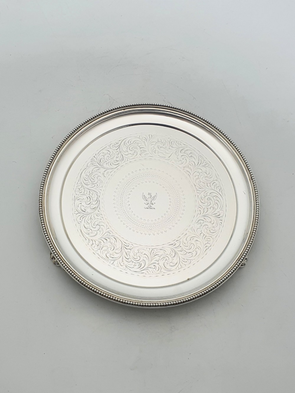 A set of three circular Victorian silver plated salvers arranged in graduated sizes, featuring beaded borders, detailed scroll engraving, and central crests. View IX