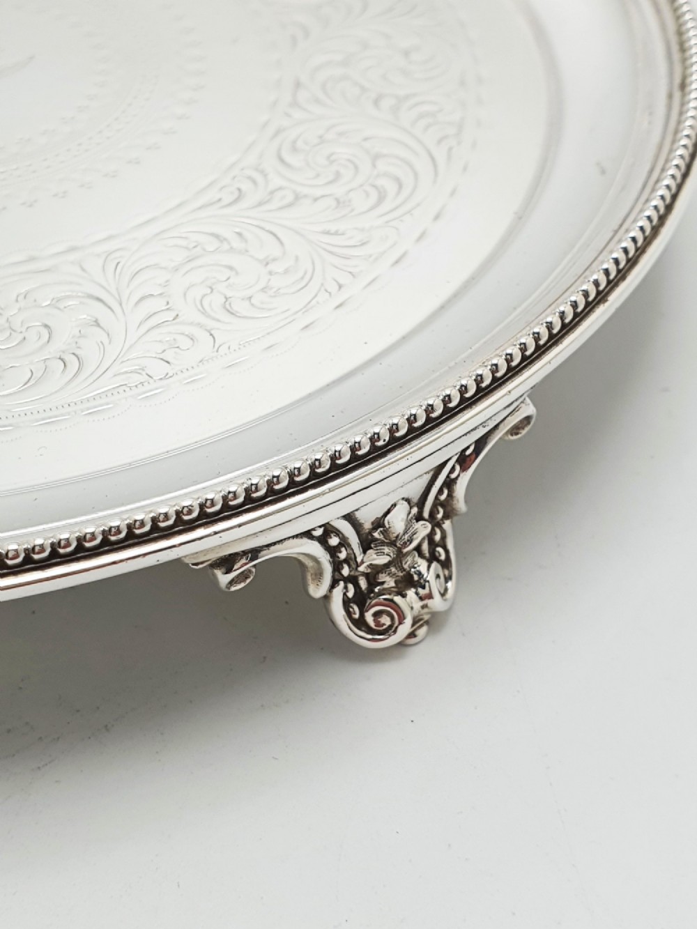 A set of three circular Victorian silver plated salvers arranged in graduated sizes, featuring beaded borders, detailed scroll engraving, and central crests. View X
