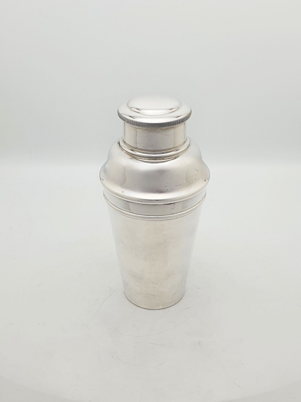 An Art Deco silver-plated cocktail shaker featuring a tapered body, stepped shoulder, and a milled-edge cap.