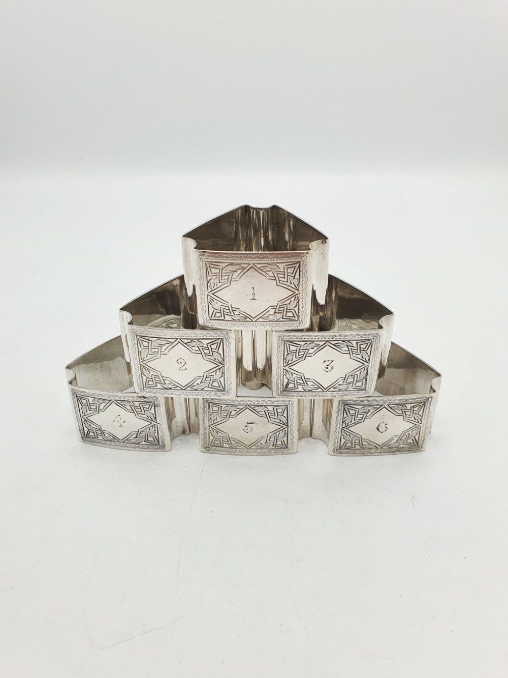 A set of six Edwardian silver-plated napkin rings numbered one through six with engraved geometric borders.