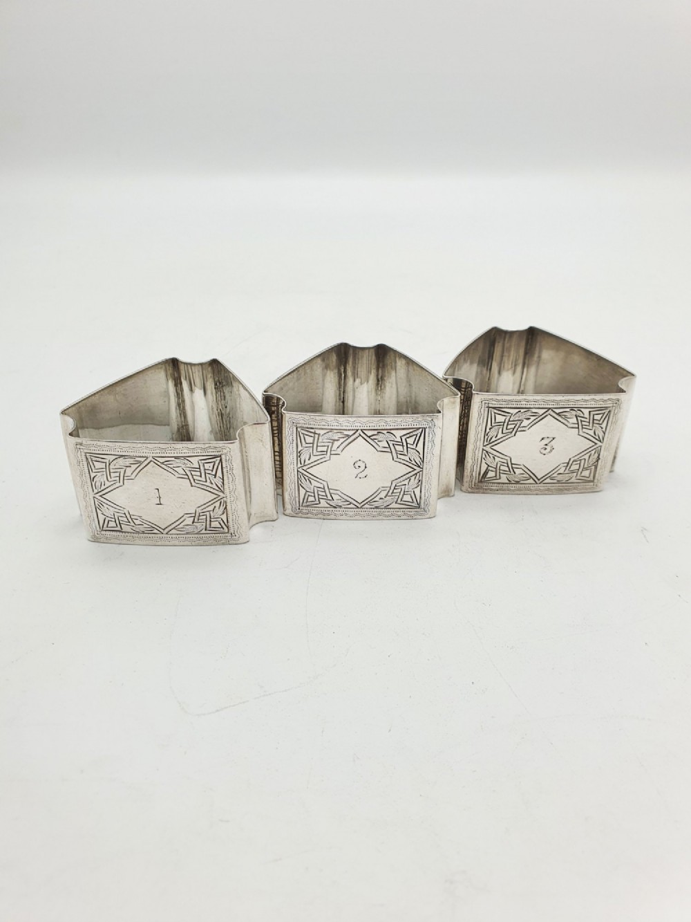 A set of six Edwardian silver-plated napkin rings numbered one through six with engraved geometric borders. View II