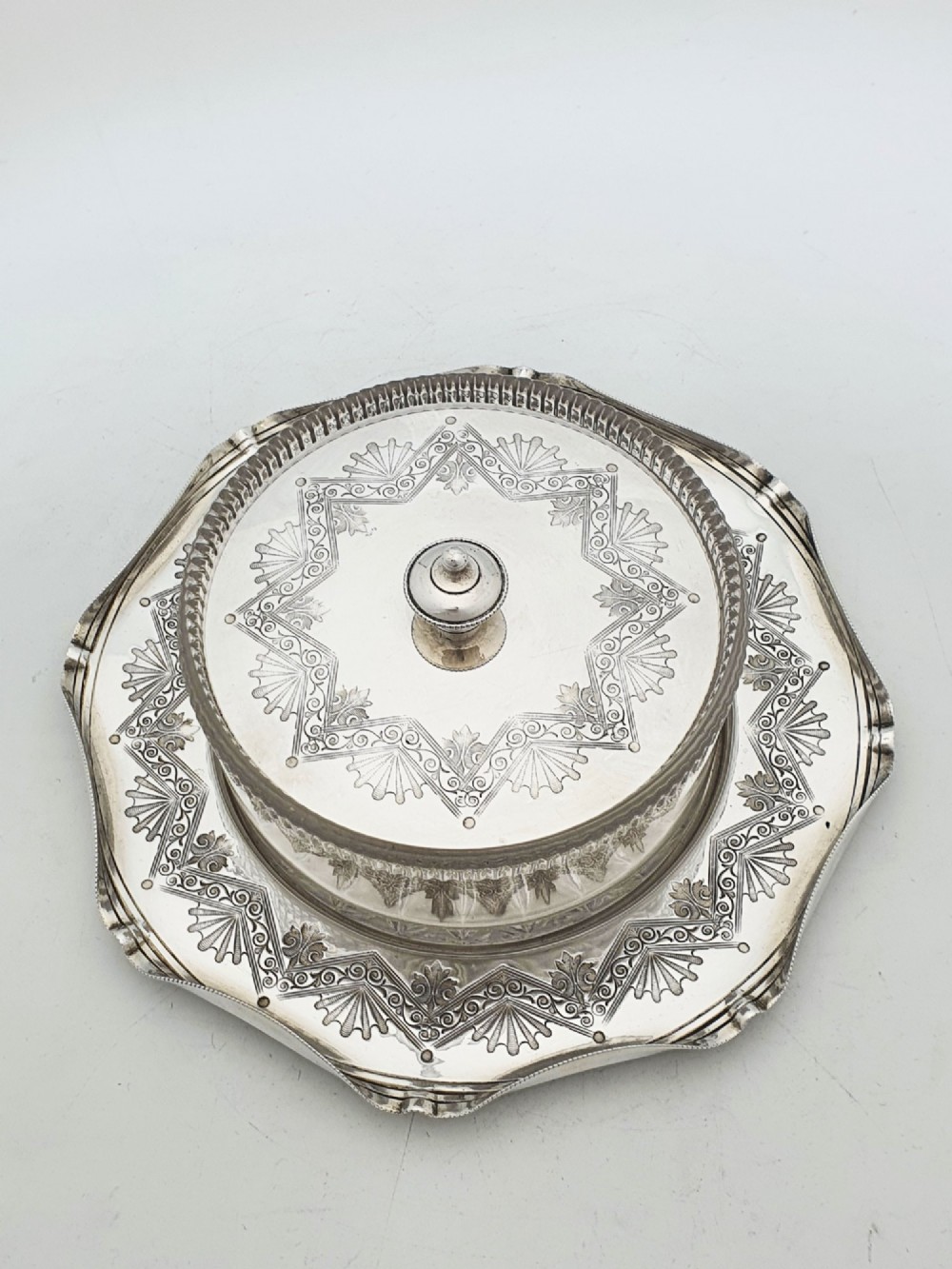 A Victorian silver-plated circular butter dish featuring bright-cut engraving and a lid with a central finial, housing a clear cut-glass liner. View II