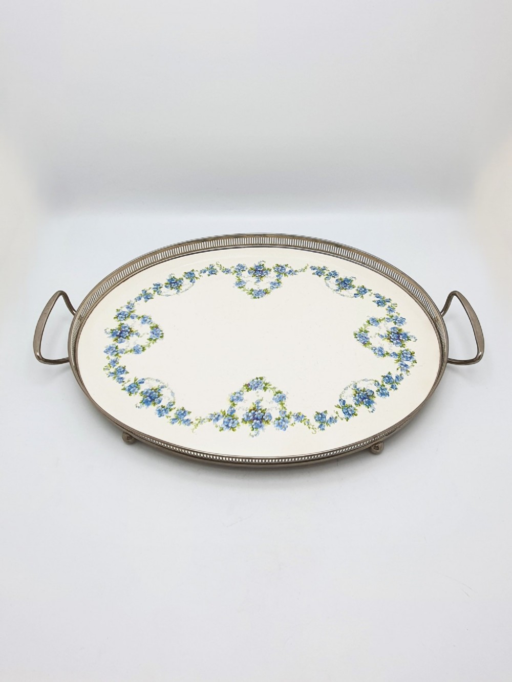 An antique oval serving tray featuring a pierced metal gallery rim, side handles, and an off-white ceramic base decorated with a blue floral garland. View IV