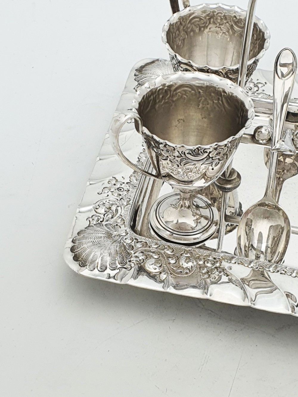 An Edwardian silver-plated egg cruet set with four embossed egg cups, four spoons, and an ornate tray with a central carry handle. View IV
