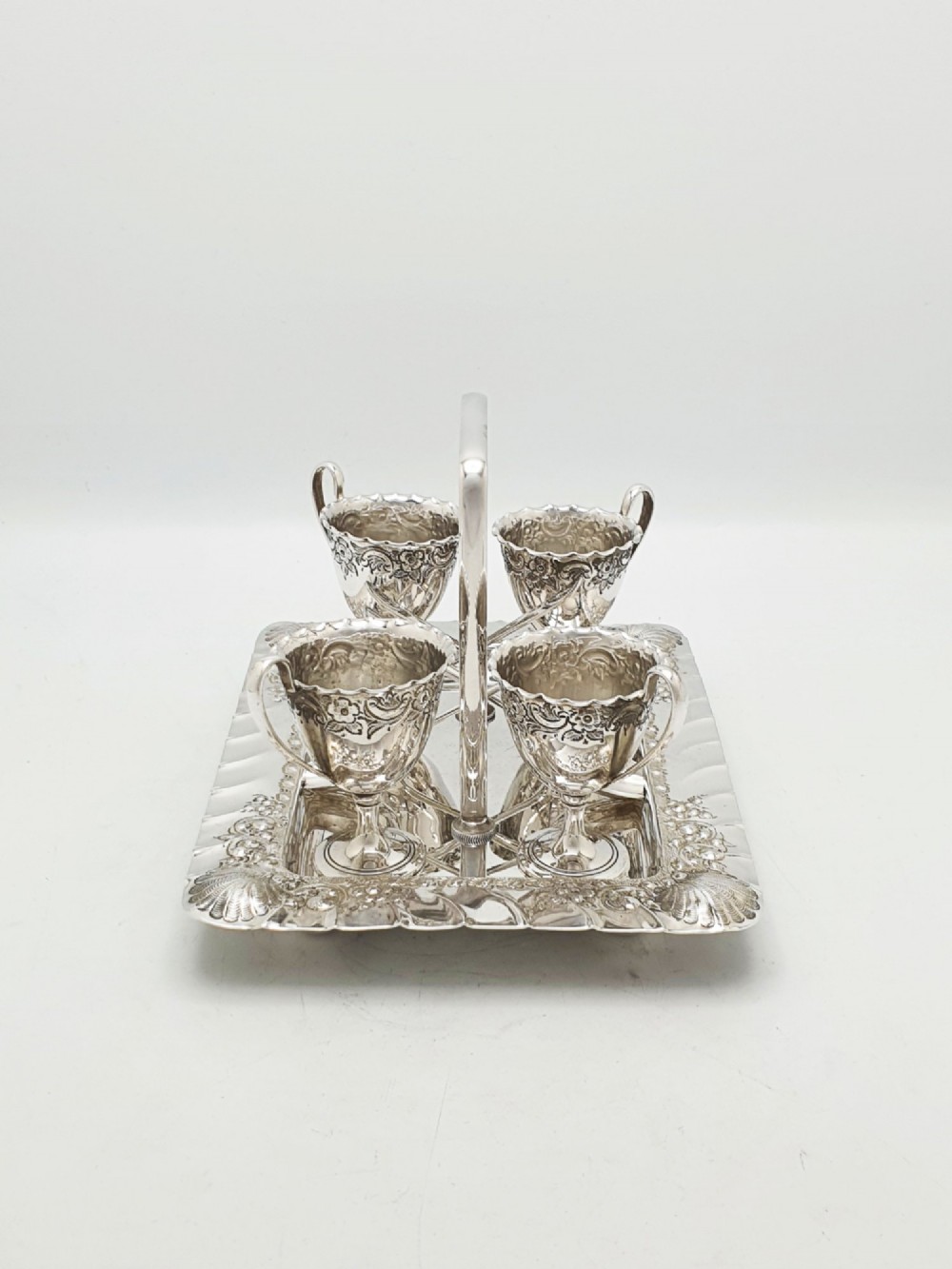 An Edwardian silver-plated egg cruet set with four embossed egg cups, four spoons, and an ornate tray with a central carry handle. View VI