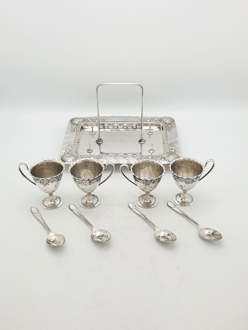 An Edwardian silver-plated egg cruet set with four embossed egg cups, four spoons, and an ornate tray with a central carry handle. View VII