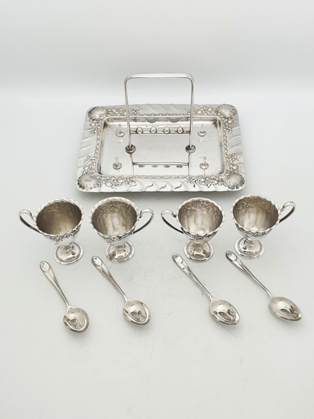 An Edwardian silver-plated egg cruet set with four embossed egg cups, four spoons, and an ornate tray with a central carry handle. View VIII