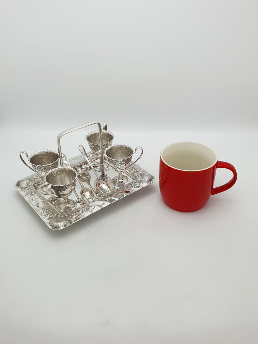 An Edwardian silver-plated egg cruet set with four embossed egg cups, four spoons, and an ornate tray with a central carry handle. View X