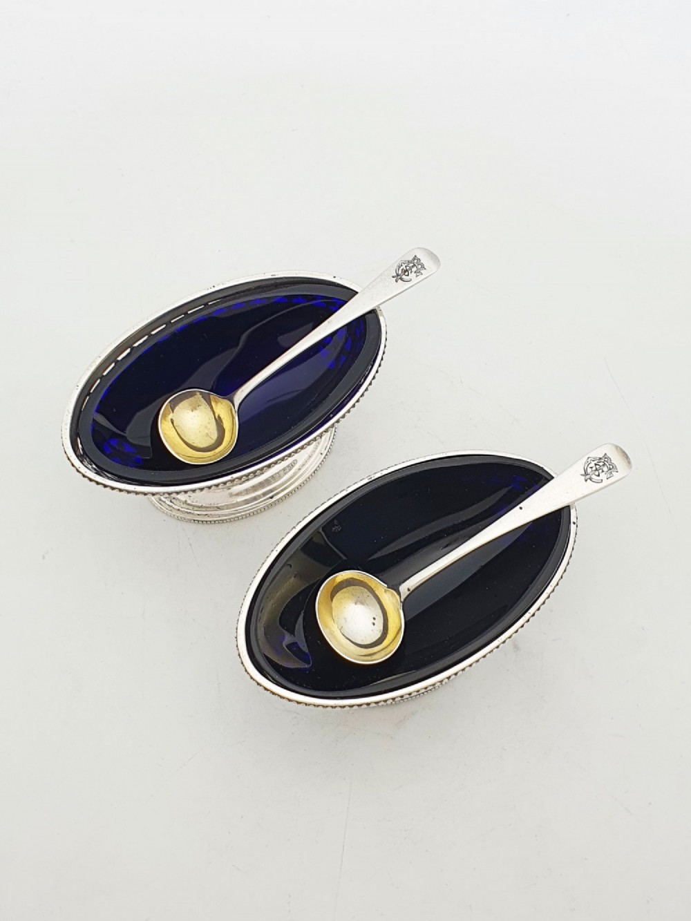 A pair of Edwardian sterling silver oval pedestal salt cellars with pierced filigree rims, dark cobalt blue glass liners, and matching silver salt spoons. View II