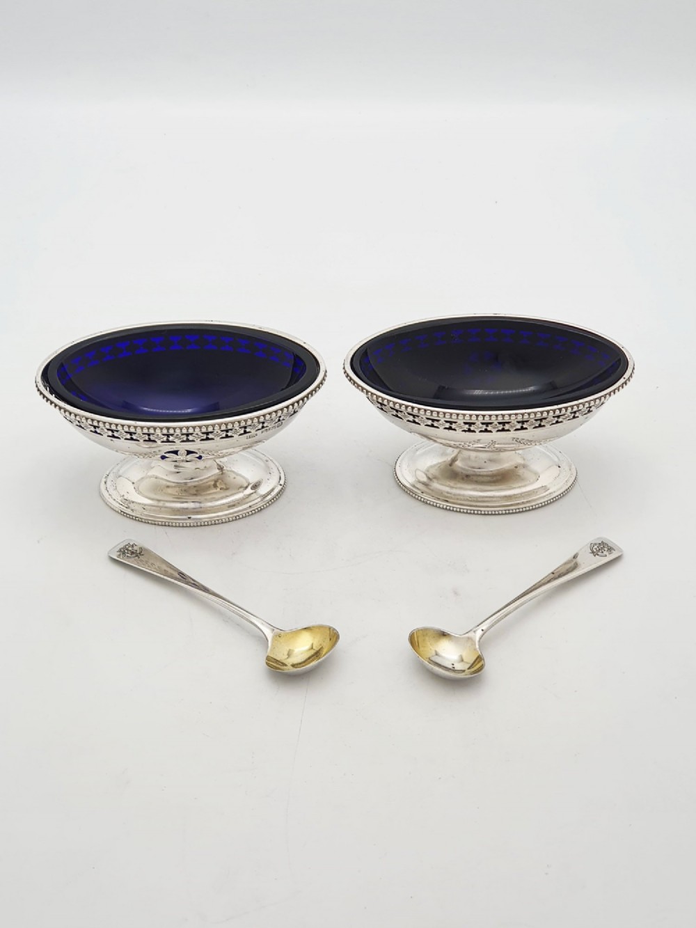 A pair of Edwardian sterling silver oval pedestal salt cellars with pierced filigree rims, dark cobalt blue glass liners, and matching silver salt spoons. View III