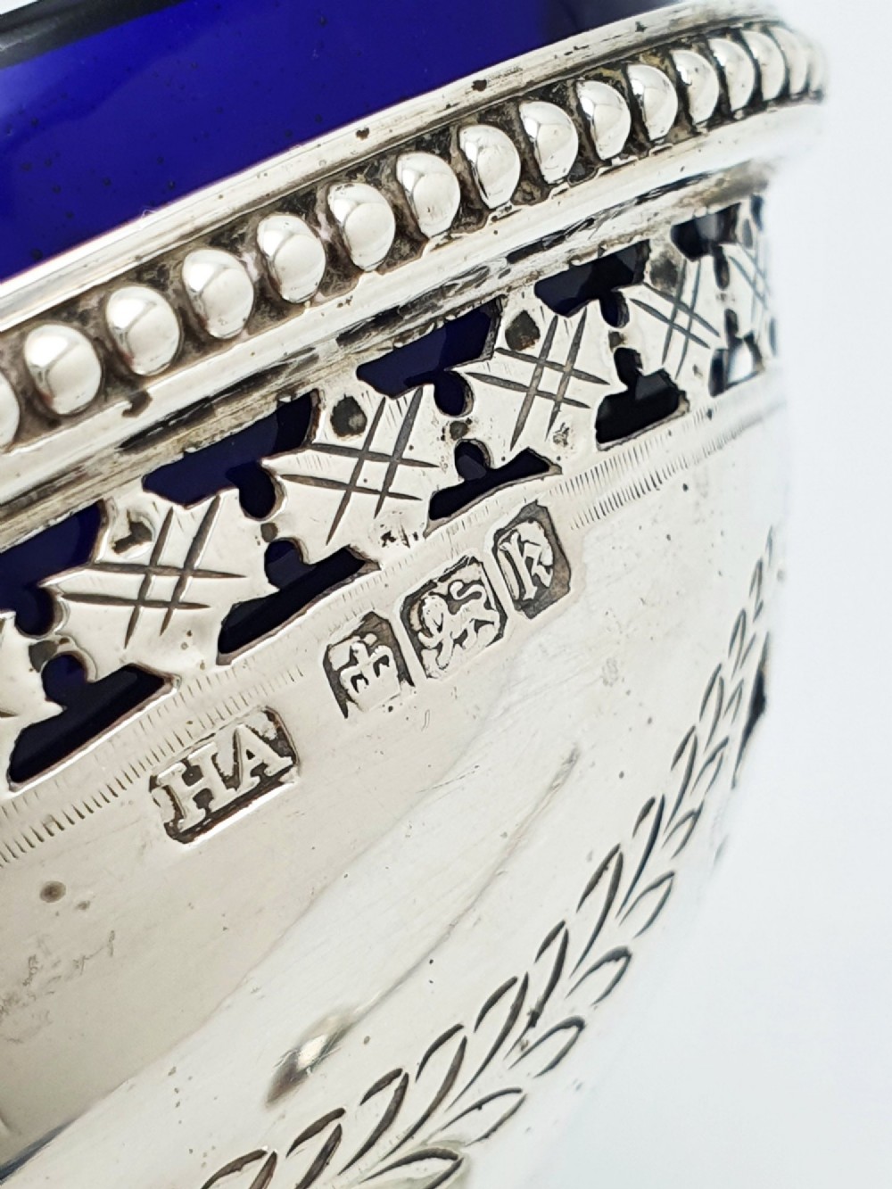 A pair of Edwardian sterling silver oval pedestal salt cellars with pierced filigree rims, dark cobalt blue glass liners, and matching silver salt spoons. View VIII
