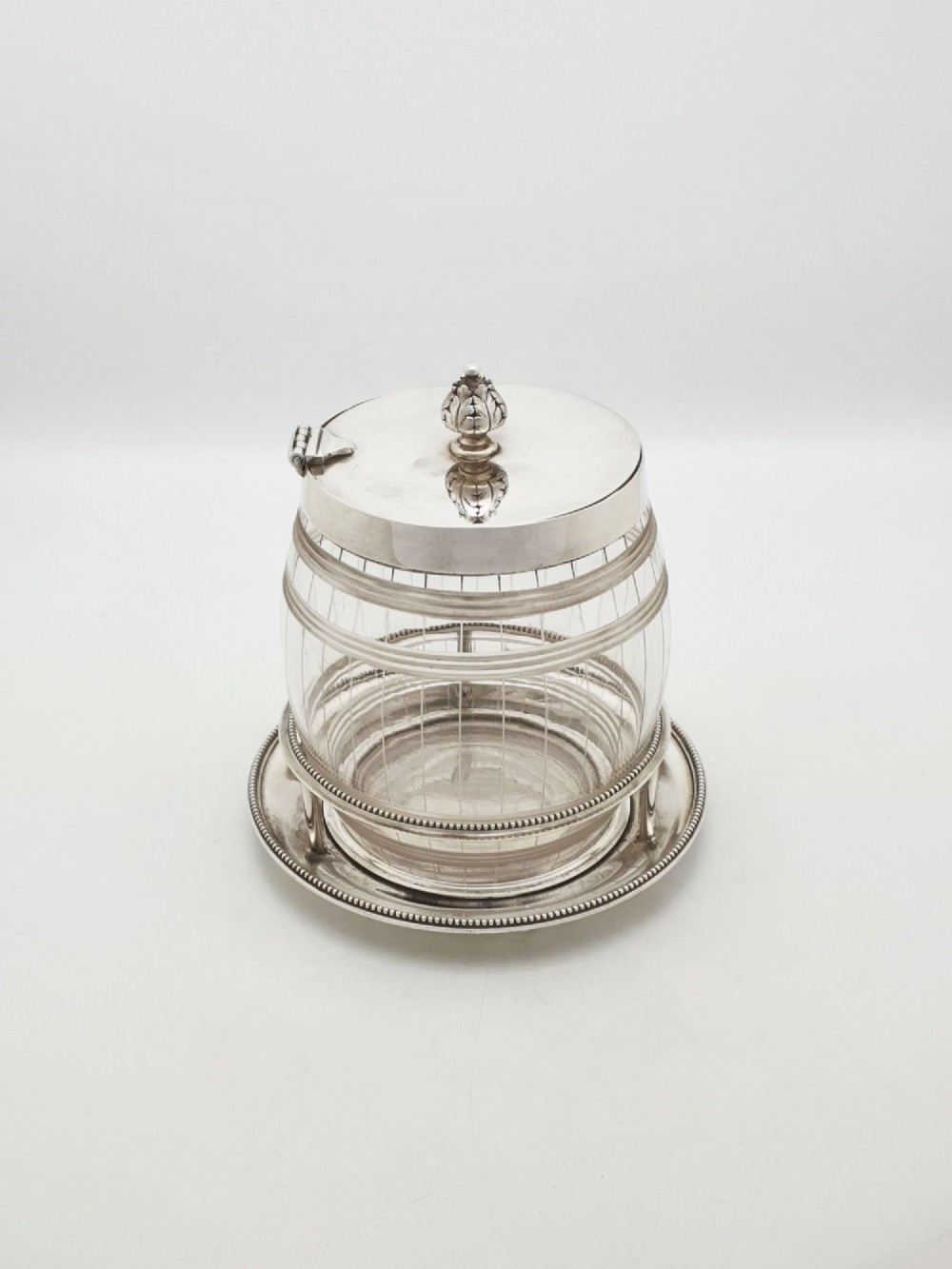 A Victorian cut glass barrel-shaped container with a silver-plated hinged lid and matching stand.