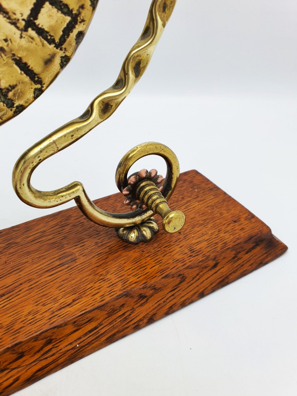 An antique brass circular gong with patterned etching suspended within a wavy brass frame on a polished rectangular oak base with a matching striker. View IV